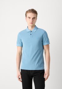 Cămașă polo de culoare albastră deschisă, cu guler, plasă cu două butoane și mâneci scurte. Prezintă un broderie subtilă a logo-ului pe piept.