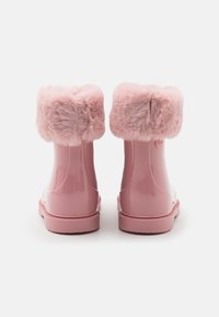 Bottes étanches roses avec une finition brillante, dotées d'un doux ourlet en fausse fourrure en haut et d'une semelle en caoutchouc pour l'adhérence.