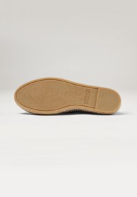 Suela de zapato de goma con una superficie texturizada, que presenta una base beige y una forma plana y desgastada. No hay patrones o marcas prominentes visibles.