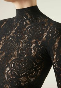 Body in pizzo nero con collo alto e motivo floreale, caratterizzato da dettagli intricati e una texture trasparente in tutto il capo.