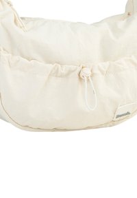 Licht beige stoffen tas met een verzamelde bovenkant, elastische trekkoordsluiting en een klein logo-label aan de zijkant. Zachte textuur en ronde vorm.
