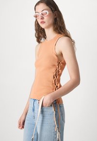Ribbet oransje tank topp med snøring på siden. Kombinert med lyseblå denim jeans og holder en stropp fra en veske.