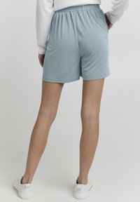 Ljusblå, stretchiga shorts med elastisk midjeresår. Slät yta och knälång design. Bärs med vita sneakers.