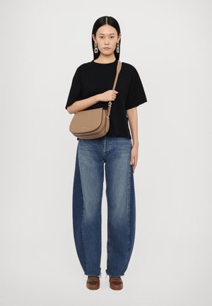Brown crossbody bag with a smooth texture, curved design, and gold hardware details, paired with oversized blue denim jeans and a black top.