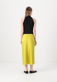 Černý plisovaný halter top v kombinaci s hedvábnou žlutou sukní ke kolenům a černými plochými botami, pohled zezadu.