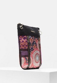 Small crossbody bag with black top, multicolored patterned fabric, two vertical front zippers, and metal rings for strap attachment.