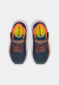 Plave atletske cipele s narančastim akcentima i bijelim potplatom. Imaju trakicu i vezice, teksturirani gornji dizajn i podstavljeni ovratnik.