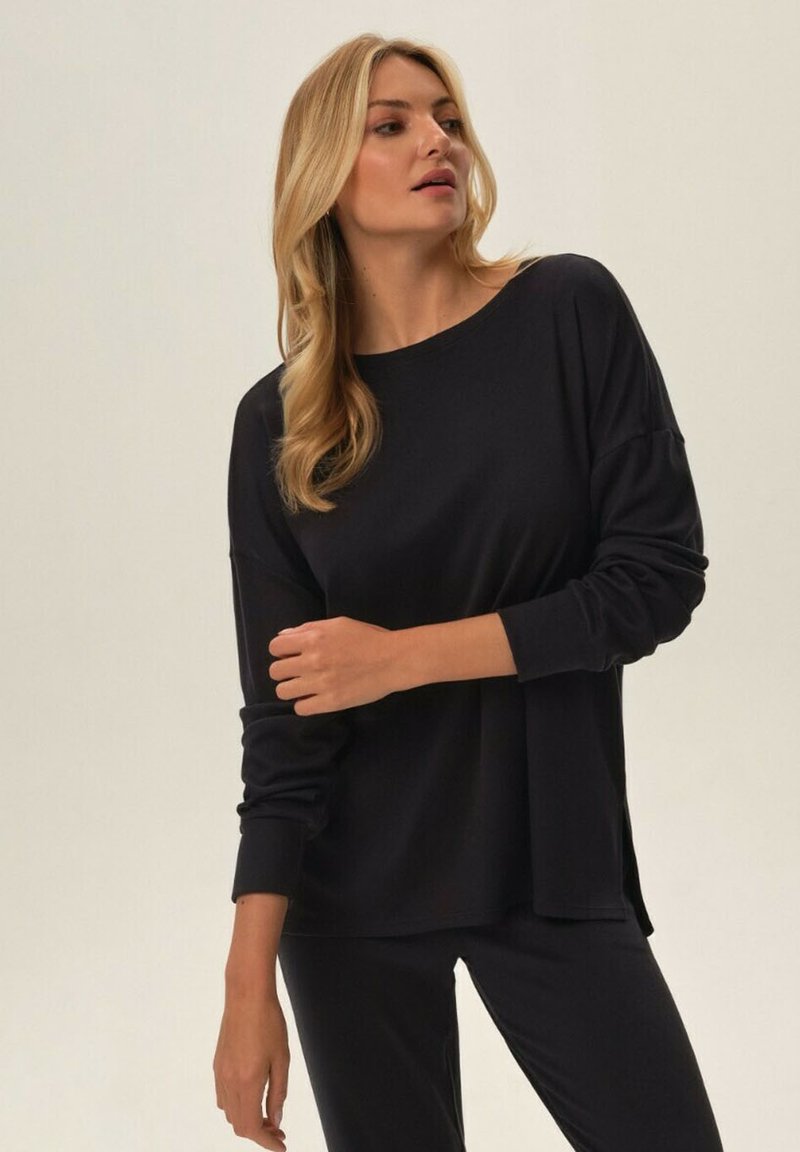 Czarny longsleeve w luźnym kroju i okrągłym dekoltem, wykonany z miękkiego materiału. W połączeniu z dopasowanymi, ciemnymi spodniami. Prosty i minimalistyczny design.