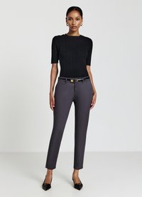 Haut noir à mailles côtelées à manches courtes associé à un pantalon ajusté gris foncé et des escarpins noirs à bout pointu, avec une ceinture fine à boucle dorée.