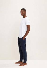 T-shirt blanc à manches courtes avec une poche sur la poitrine, associé à un pantalon de jogging bleu marine avec des poignets aux chevilles et des poches latérales.