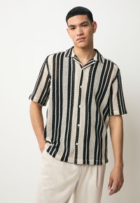 Camisa de manga corta con botones, con rayas verticales en negro y crema, confeccionada en un tejido de punto texturizado con un ajuste holgado.