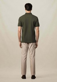 Tmavě zelené polo tričko s límcem, které je kombinováno se světle béžovými cargo kalhotami se bočními kapsami. Model stojí na neutrálním pozadí.