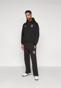 Black hoodie and matching pants made of fleece fabric. Hoodie features red and white embroidered logos and a kangaroo pocket.