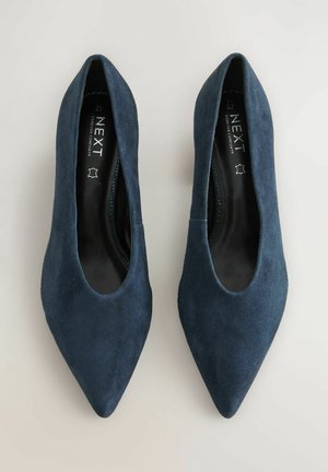 Mörkblå mocka pumps med spetsig tå, som har en slät yta och en minimalistisk design. Innerfoder i en kontrasterande svart färg.