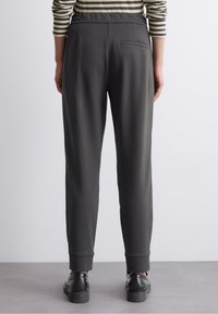 Pantalones deportivos grises con pierna cónica, cintura elástica y un solo bolsillo trasero. Textura suave con puños acanalados en los tobillos.