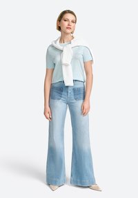 Tricou bleu deschis asortiat cu blugi din denim decolorat, cu talie înaltă și croi larg. O pulover alb tricotat este aruncat pe umeri.