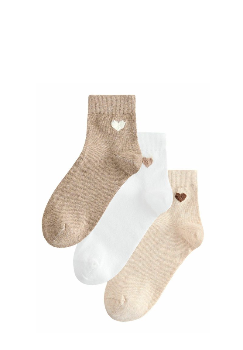 Tre par korta strumpor: en beige med vit hjärta, en vit med beige hjärta, och en ljusbeige. Mjuk stickad textur.
