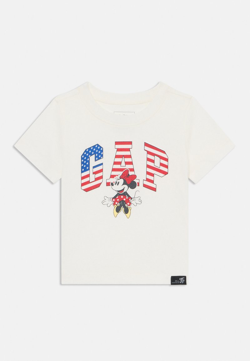 Kreminė trumpomis rankovėmis marškinėliai su raudona, balta ir mėlyna 'GAP' logotipu, kuriame pavaizduotas animacinis personažas su taškuota suknele.