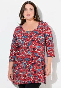 Punainen tunika, jossa on 3/4-hihat, sinivalkoisella kukka- ja paisley-kuviolla sekä pyöreä pääntie.