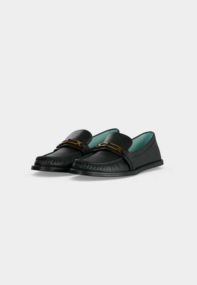 Ζευγάρι μαύρα δερμάτινα loafers με χρυσή μεταλλική αγκράφα και ανοιχτό μπλε εσωτερική επένδυση, εμφανίζονται σε λευκό φόντο.