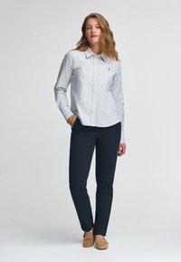 Camicia a righe button-up in cotone blu chiaro e bianco, abbinata a pantaloni blu scuro e mocassini color tan, con colletto classico e vestibilità attillata.