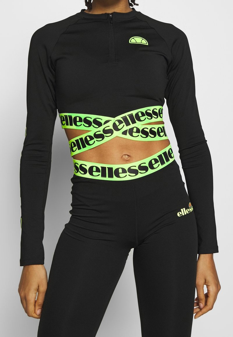 Svart långärmad crop top med blixtlås, med reflekterande neongrön branding och detaljer. Stretchigt material, åtsittande design.