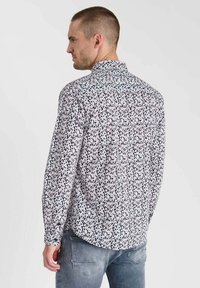 Chemise à manches longues avec un motif floral noir et blanc, dotée d'un col pointu et d'une fermeture à boutons sur le devant. Le matériau semble léger et lisse.