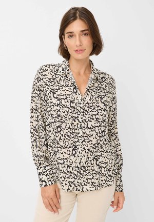 Chemise beige à manches longues avec un imprimé léopard noir, présentant un col, une fermeture à boutons et une coupe décontractée. Texture de tissu léger.