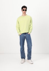 Light green long-sleeve shirt, denim jeans, white sneakers, and black sunglasses. Simple design, relaxed fit, and cotton texture.