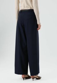 Marineblauwe wijde broekspijpen gemaakt van een gladde stof, met een hoge taille, zijzakken en een strakke achterkant zonder zichtbare sluitingen.