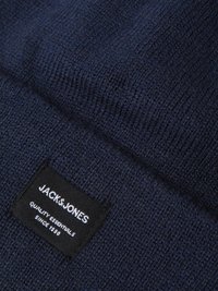 Berretto in maglia blu navy caratterizzato da un motivo testurizzato e un'etichetta nera con testo bianco, che riporta "JACK & JONES" e "QUALITY ESSENTIALS SINCE 1990."