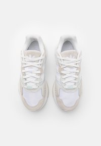 Vita atletiska sneakers i vitt med mocka- och textilpaneler, med snörning, vadderad krage och tre horisontella ränder.