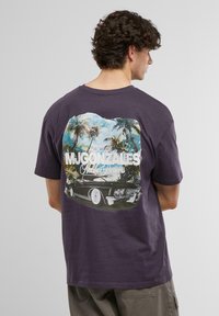 Lilla bomull t-skjorte med et vintage grafisk design av en bil og palmer på baksiden, med hvit tekst som sier "MJ Gonzales Malibu Dreamers."
