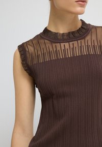 Brązowy, prążkowany top bez rękawów z przezroczystą, plisowaną karczką. Posiada okrągły dekolt z delikatnie falbaniastymi krawędziami, eksponując różnorodne tekstury.