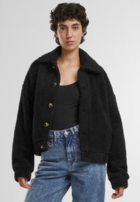 Zwarte fleecjas met een kraag, knoopsluiting en een oversized pasvorm. Heeft een zachte textuur en opvallende stiksels.