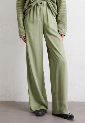 Light green wide-leg pants made of smooth fabric, featuring an elastic waist and pleats, paired with black flat shoes.