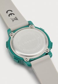 Boîtier de montre en plastique vert avec un fond en acier inoxydable argenté, bracelet en silicone gris et vis apparentes. Résistant à l'eau jusqu'à 5 ATM.