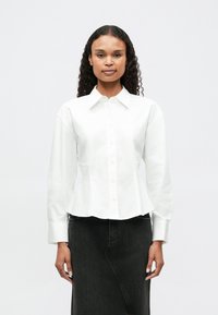 White button-up shirt with a fitted waist, long sleeves, and a collar, paired with a black denim skirt. Smooth texture, minimalistic design.
