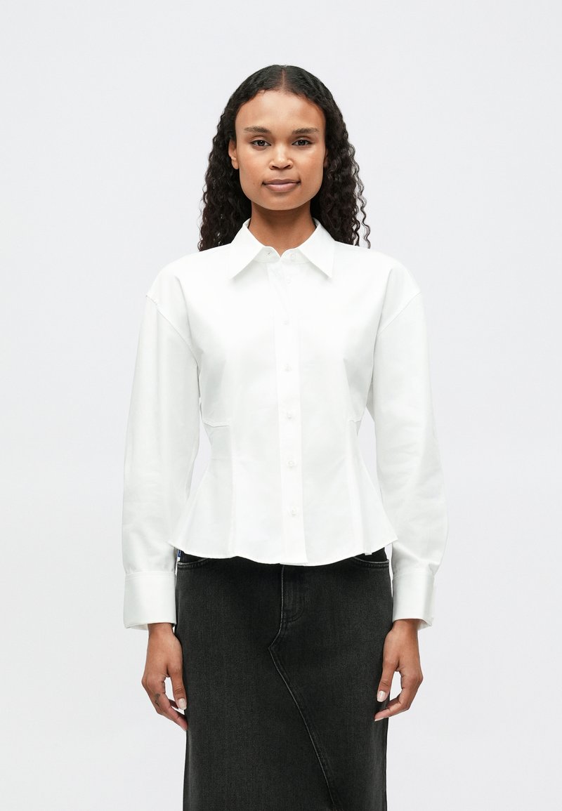 White button-up shirt with a fitted waist, long sleeves, and a collar, paired with a black denim skirt. Smooth texture, minimalistic design.