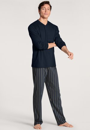 Haut à manches longues bleu marine associé à un pantalon de pyjama rayé. Le pantalon présente des rayures verticales en bleu, vert et blanc, fabriqué en tissu léger.