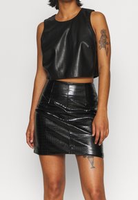 Svart beskuren ärmlös topp i mjuk konstläder, parat med en högmidjad svart pennkjol med krokodiltextur.