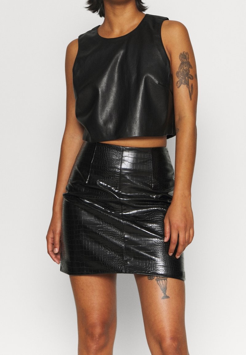 Svart beskuren ärmlös topp i mjuk konstläder, parat med en högmidjad svart pennkjol med krokodiltextur.