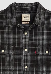 Black and white plaid shirt with short sleeves, relaxed fit, two chest pockets, and white buttons; features a Levi's tag in the collar.