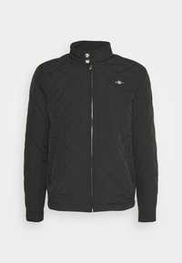 Black quilted jacket with high collar, featuring a front zipper, snap buttons, and a small logo on the chest. Smooth texture throughout.