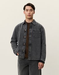 Mørk grå denimjakke for menn med knapplukking, spiss krage, brystlomme og lange ermer, brukt over en brun strikket genser.