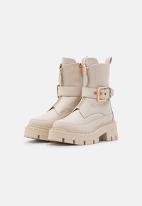 Botines beige hechos de cuero suave, con una suela de plataforma gruesa, doble cremallera y detalles de una correa ajustable con hebilla.