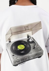 Hvit t-skjorte med et grafisk motiv av en vintage platespiller med en svart vinylplate og gul etikett, detaljert med knotter og et gjennomsiktig deksel.