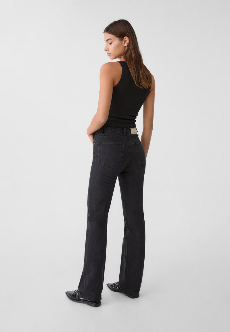 Jeans noirs évasés avec une texture lisse, des poches arrières et des coutures légères ; associés à un débardeur noir ajusté et des chaussures plates.