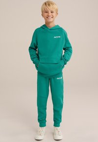 Ensemble en sweat vert et pantalon assorti en tissu doux, doté d'une capuche, d'une poche avant et d'un logo brodé sur la poitrine et la jambe du pantalon.