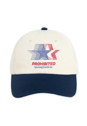 Jonge man die een beige en marineblauwe pet draagt met een vlaglogo, een marineblauwe jas met borduursel "Modern Yuppies" en een grijs overhemd met een rood en blauw ontwerp.